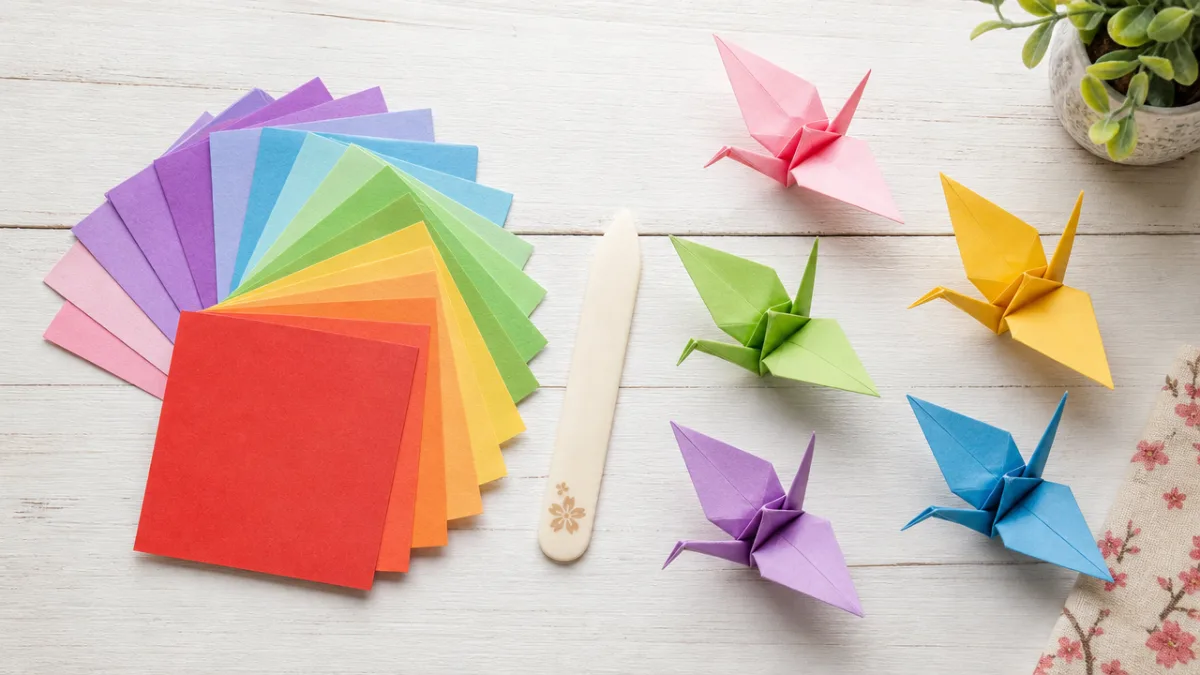 a neatly arranged flat lay of colorful origami paper squares, bone folder,…