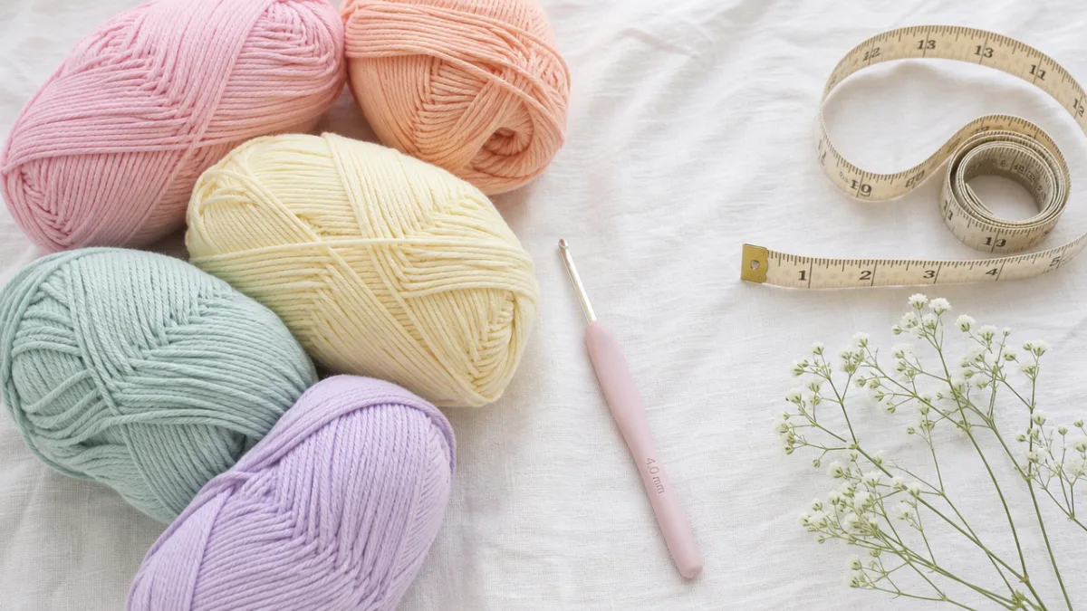 a flat lay of pastel cotton yarn skeins, a crochet hook, and…