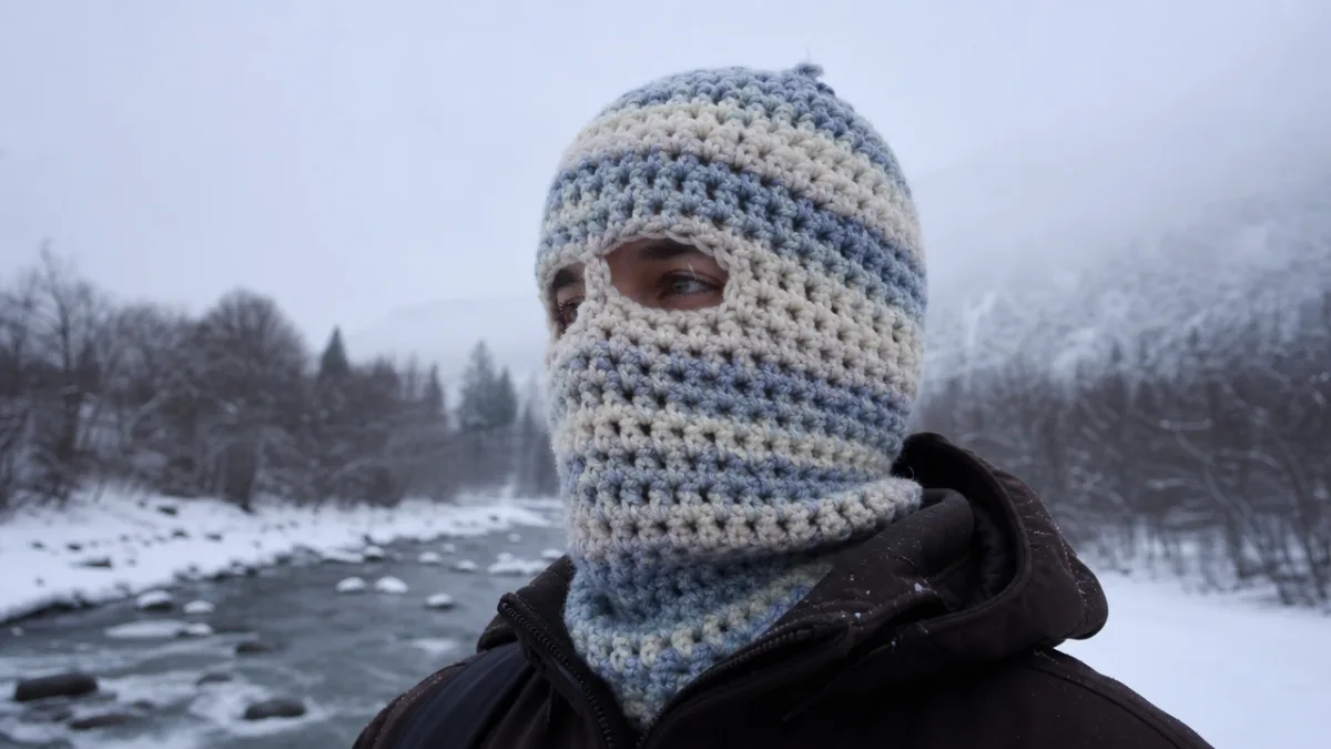 a person wearing a chunky handmade crochet balaclava outdoors in winter snow,…