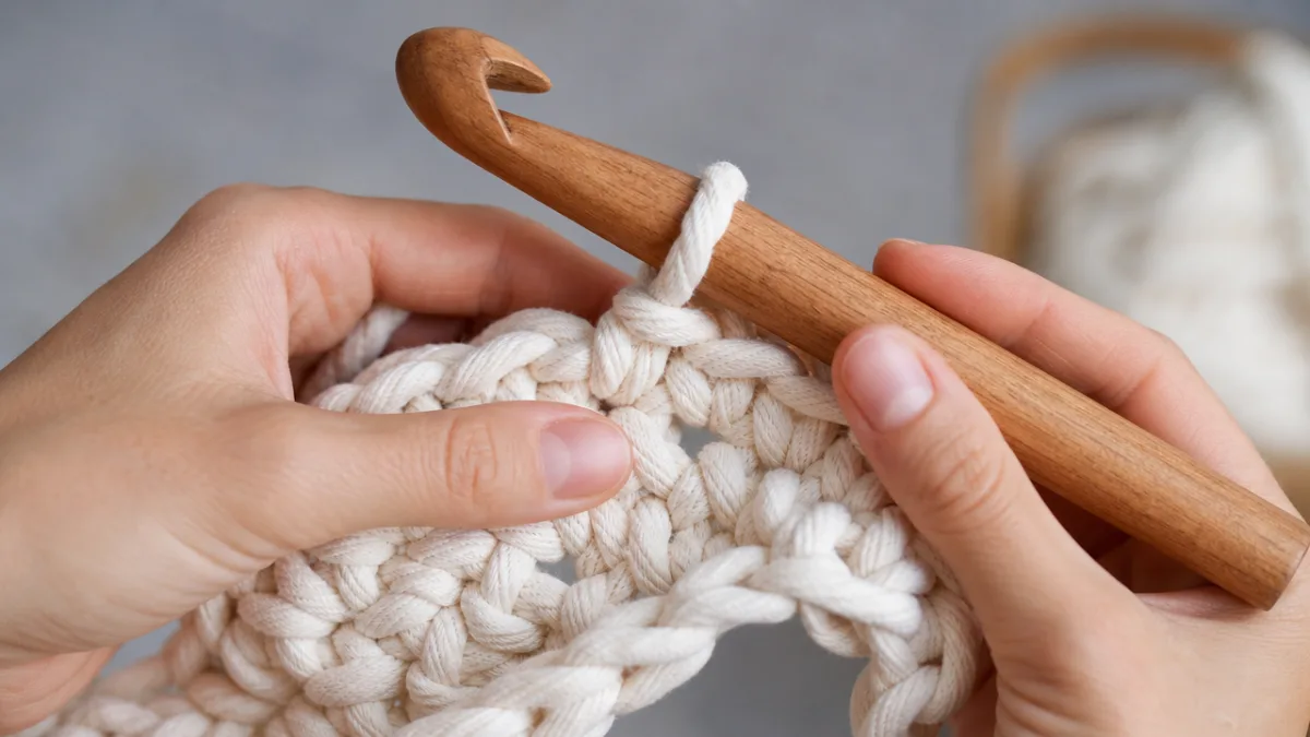 close-up of hands crocheting thick white rope with an oversized wooden hook,…