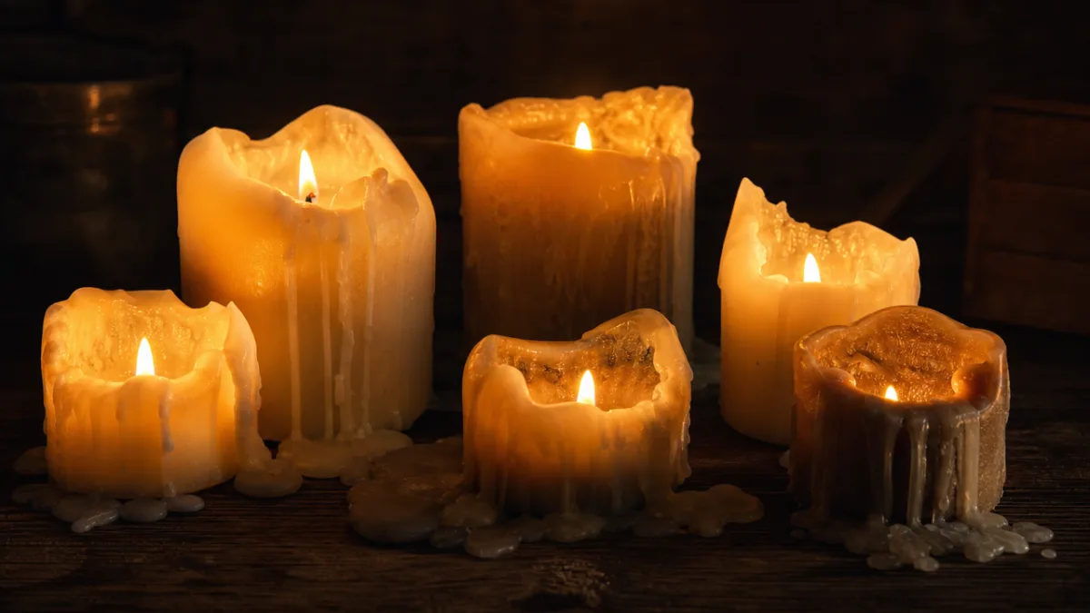 a collection of melted pillar candles on a dark wooden surface, warm…