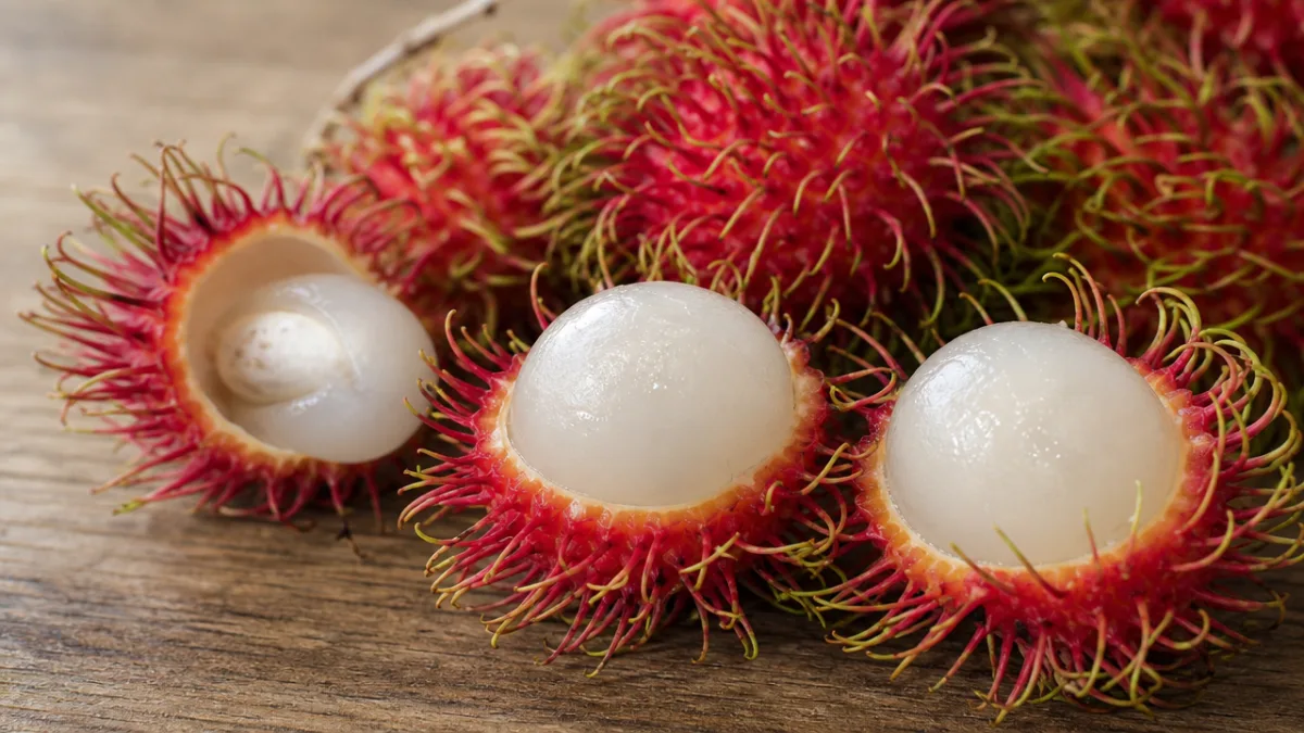 a close-up of fresh rambuttan fruits cut open showing translucent white flesh,…