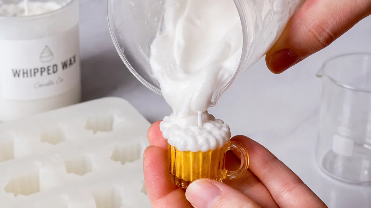 close-up of hands pouring white whipped wax foam onto a tiny golden…