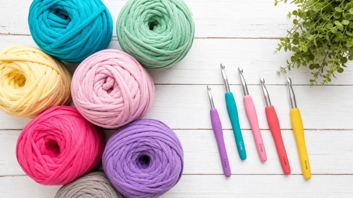 a flat lay of colorful t-shirt yarn skeins and crochet hooks on…
