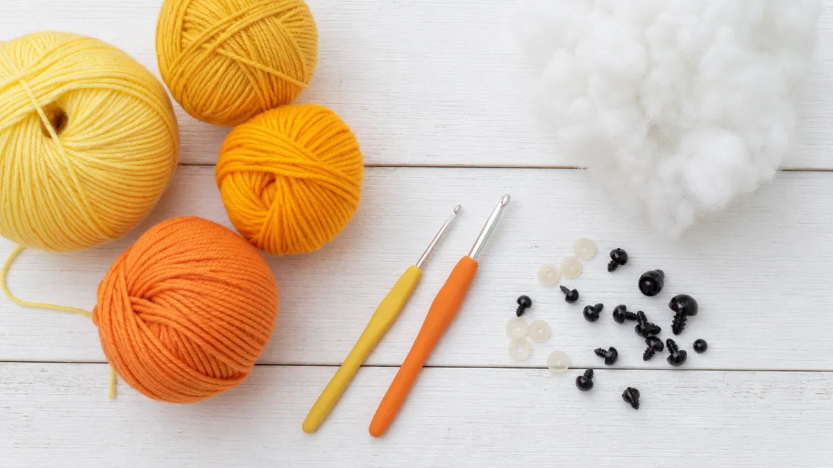 a flat lay of yellow and orange yarn balls, crochet hooks, safety…