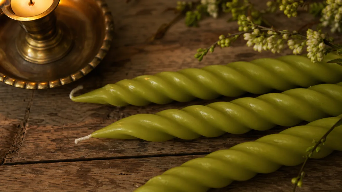 a close-up of spring green twisted taper candles on a rustic wooden…