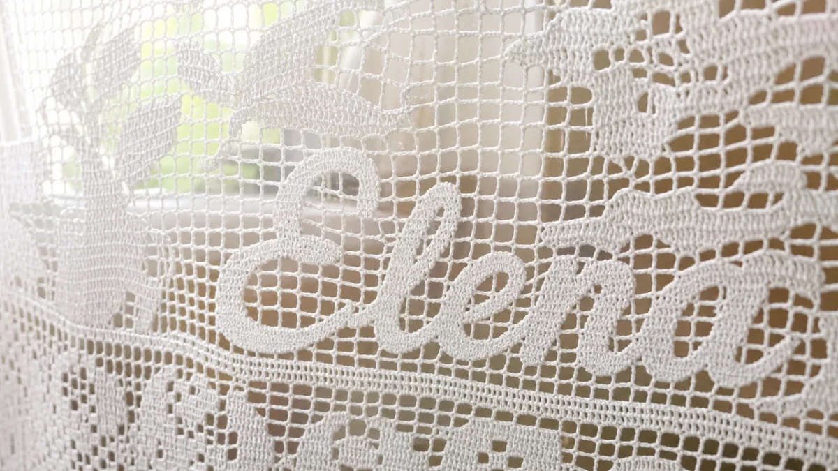a close-up detail of fine white crochet lacework with visible name lettering,…