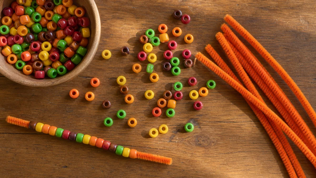 a flat lay of colorful pony beads and orange pipe cleaners arranged…
