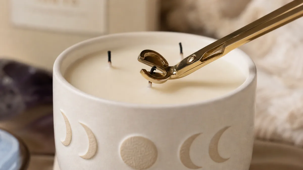 a close-up of a moon phase candle wick being trimmed with a…