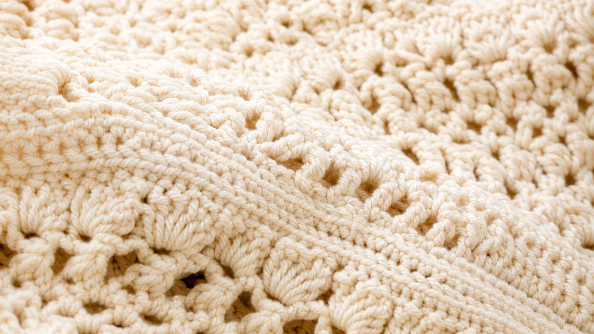 a close-up of textured crochet fabric in soft ivory yarn, warm studio…