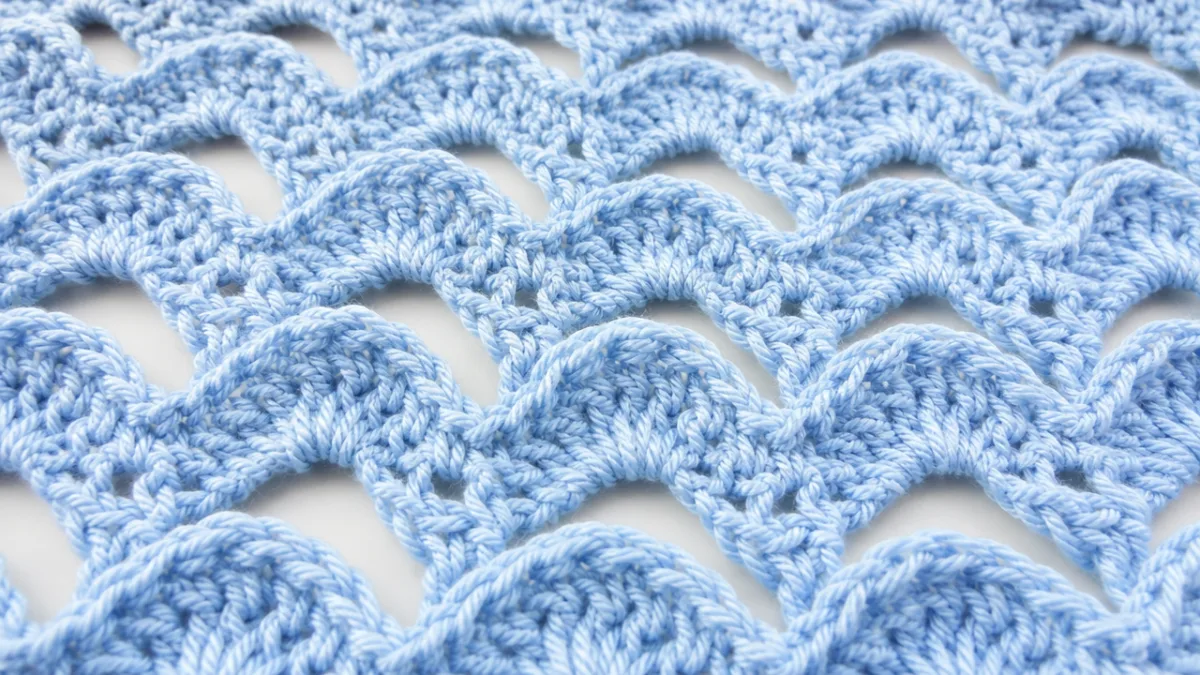 close-up of open wave crochet stitch texture in pale blue yarn, bright…