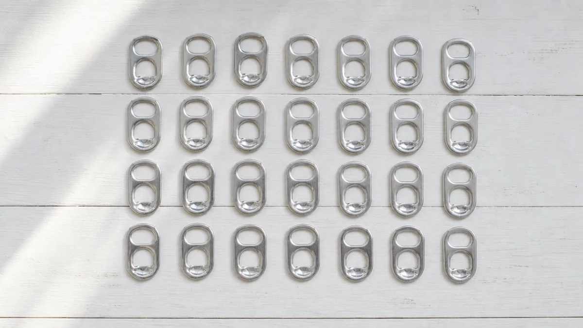 a flat lay of shiny aluminum pop tabs arranged neatly on a…