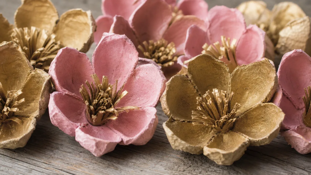 close-up of handmade egg carton flowers in pink and gold tones on…