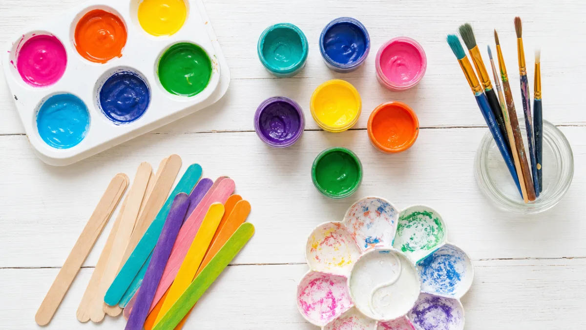 a flat lay of colorful paints, brushes, and popsicle sticks on a…