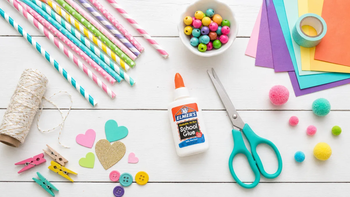 a flat lay of colorful paper straws, scissors, glue, and craft supplies…
