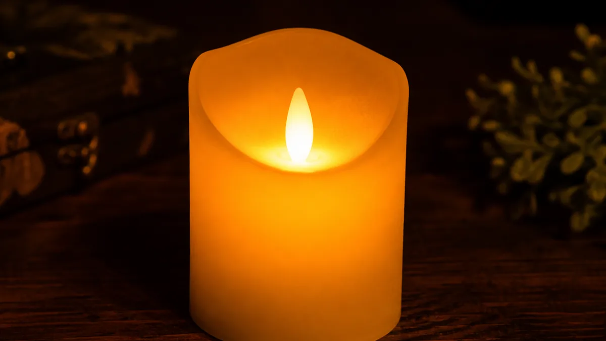 a close-up of a glowing flameless pillar candle on a dark wooden…