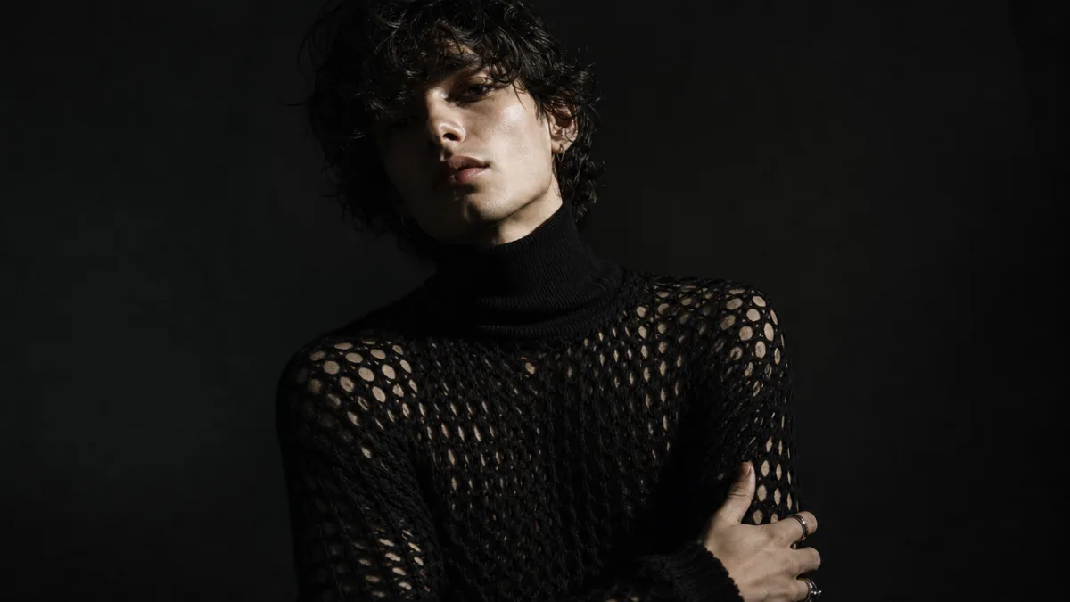 a person wearing a black fishnet crochet sweater over a turtleneck, dramatic…