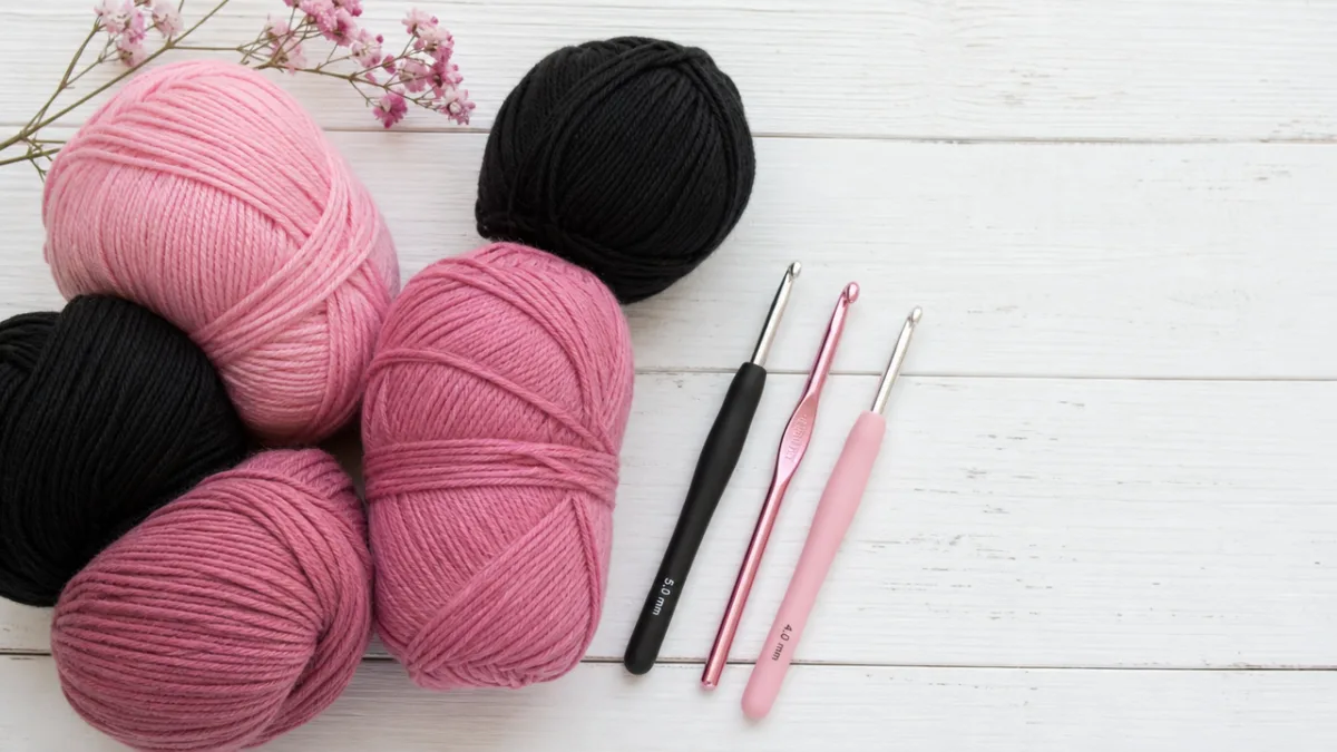 a flat lay of pink and black yarn skeins alongside crochet hooks…