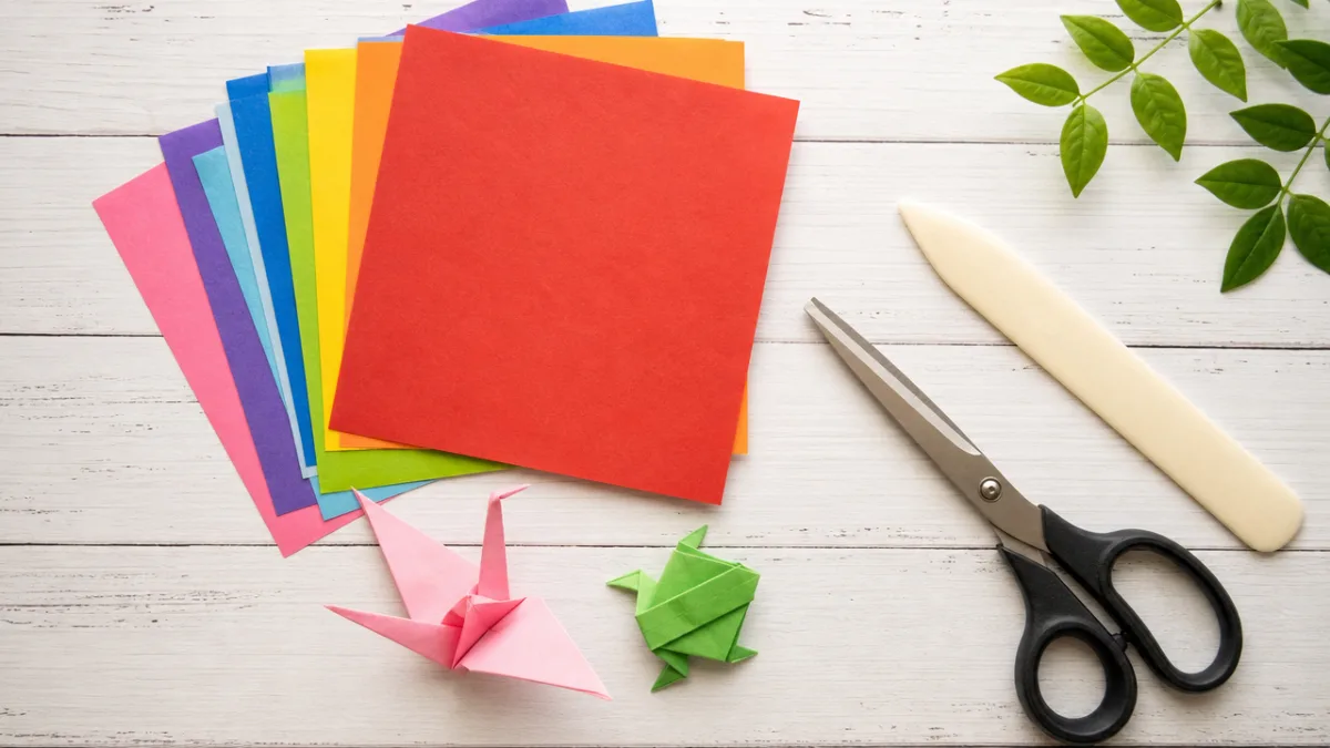 flat lay of colorful origami paper squares, scissors, and a bone folder…