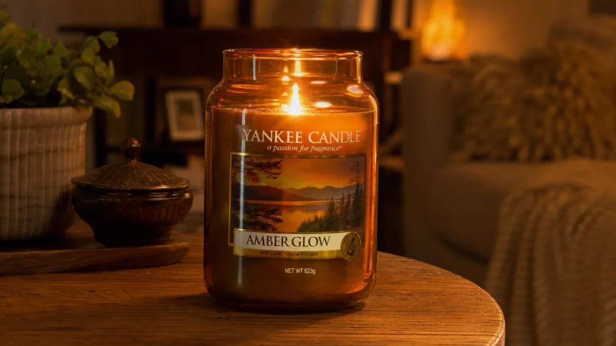 a large amber glass Yankee Candle jar glowing warmly on a wooden…