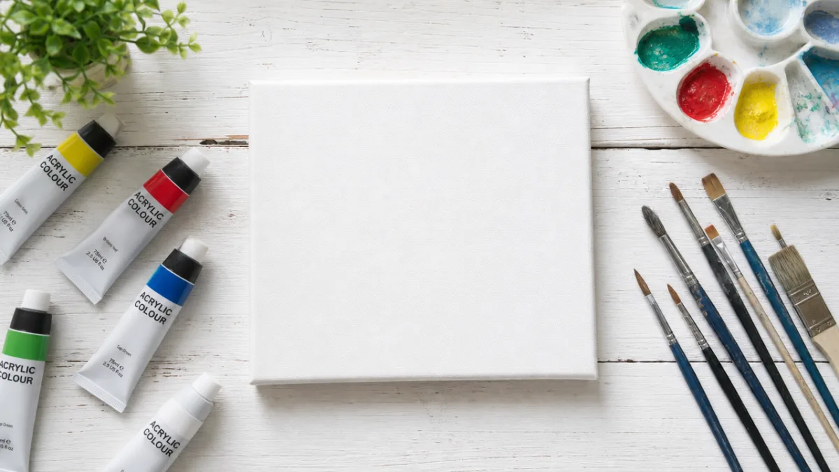 a flat lay of acrylic paints, brushes, and a blank canvas on…