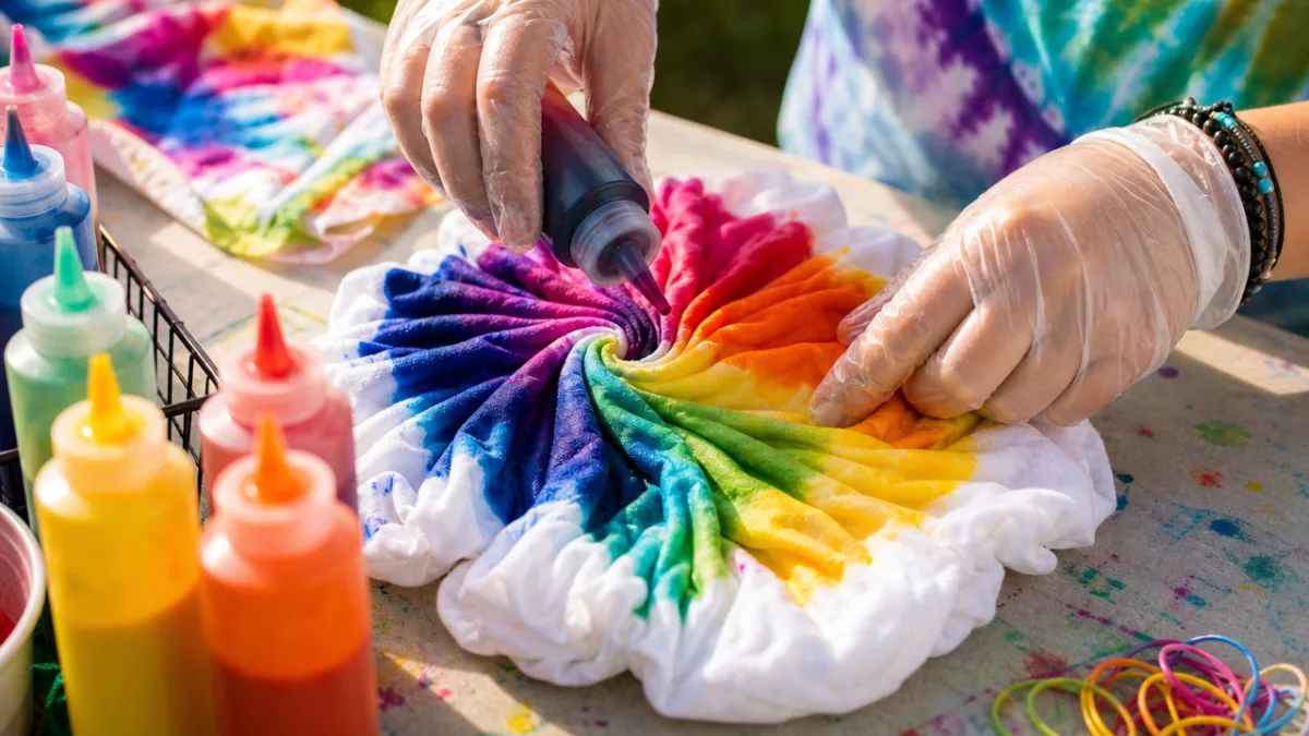 close-up of hands applying vibrant tie-dye colors to white fabric on a…