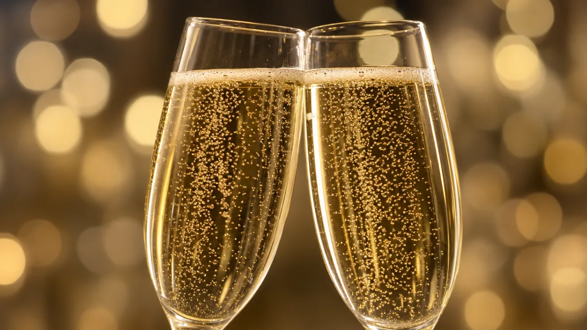 close-up of two champagne flutes clinking together with golden bubbles rising, bokeh…
