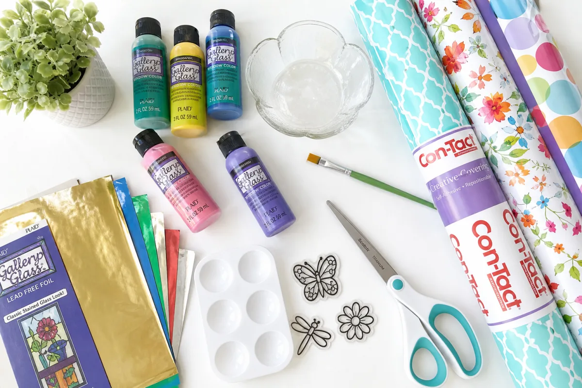 flat lay of colorful craft supplies including glass paints, contact paper, and…